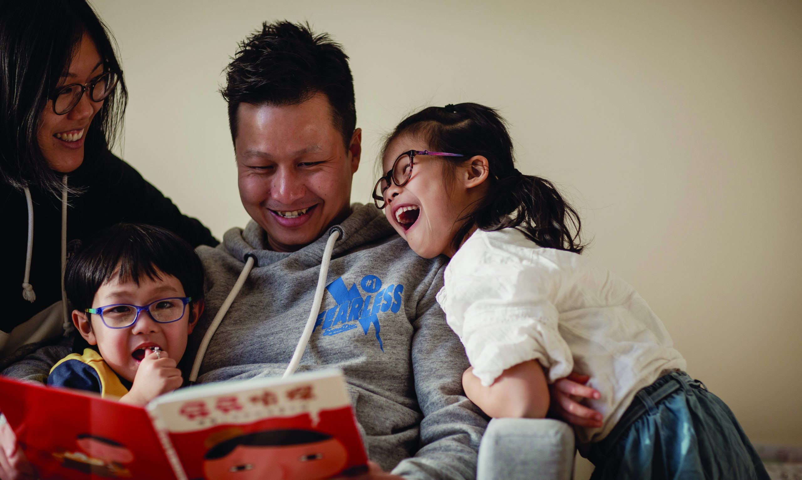 Family of young girl, young boy, male and female laughing reading a book